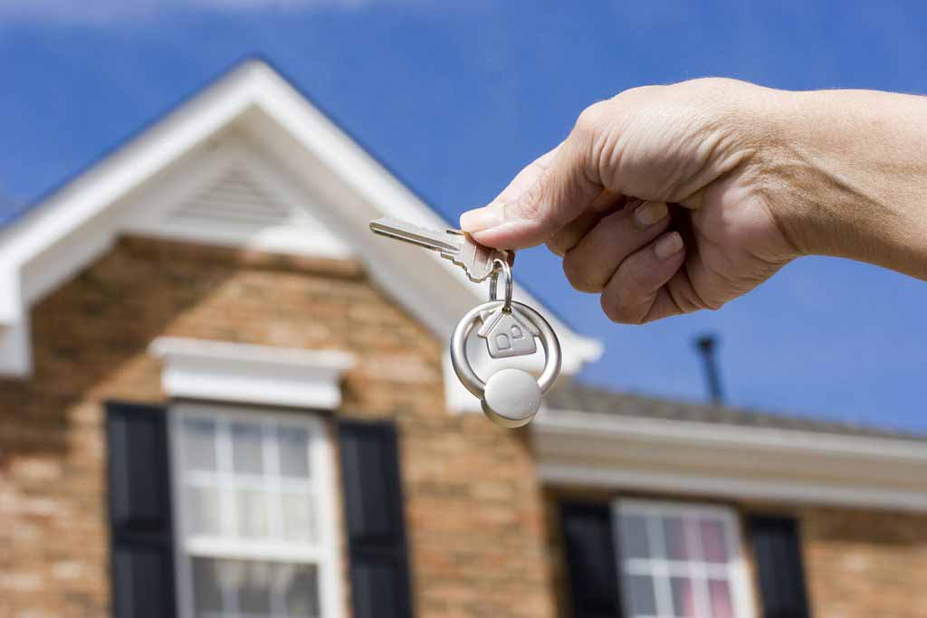 hand holding house keys in front of house